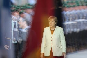 Angela Merkel hinter einer Glasscheibe im Spiegel von Bundeswehrsoldaten
